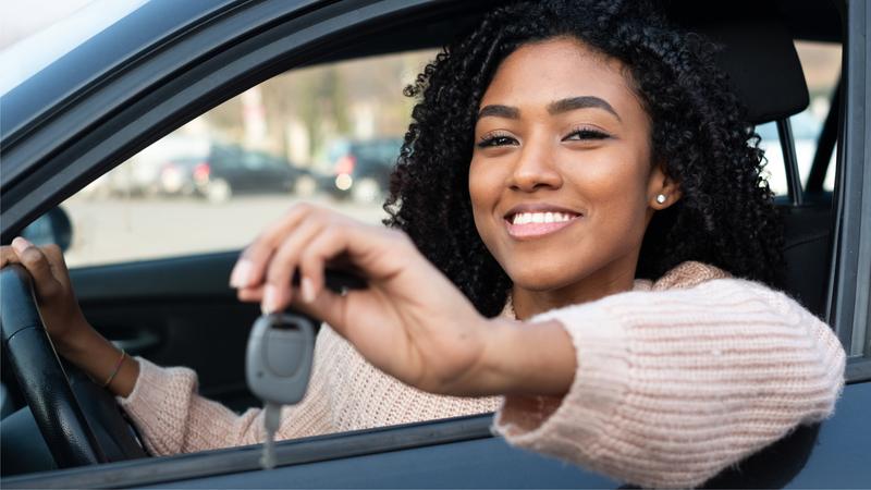 Smiling young female driver holding keys while sitting in car